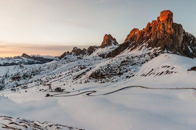 Schneebedeckte Berglandschaft mit kurviger Straße und Felsen im Abendlicht